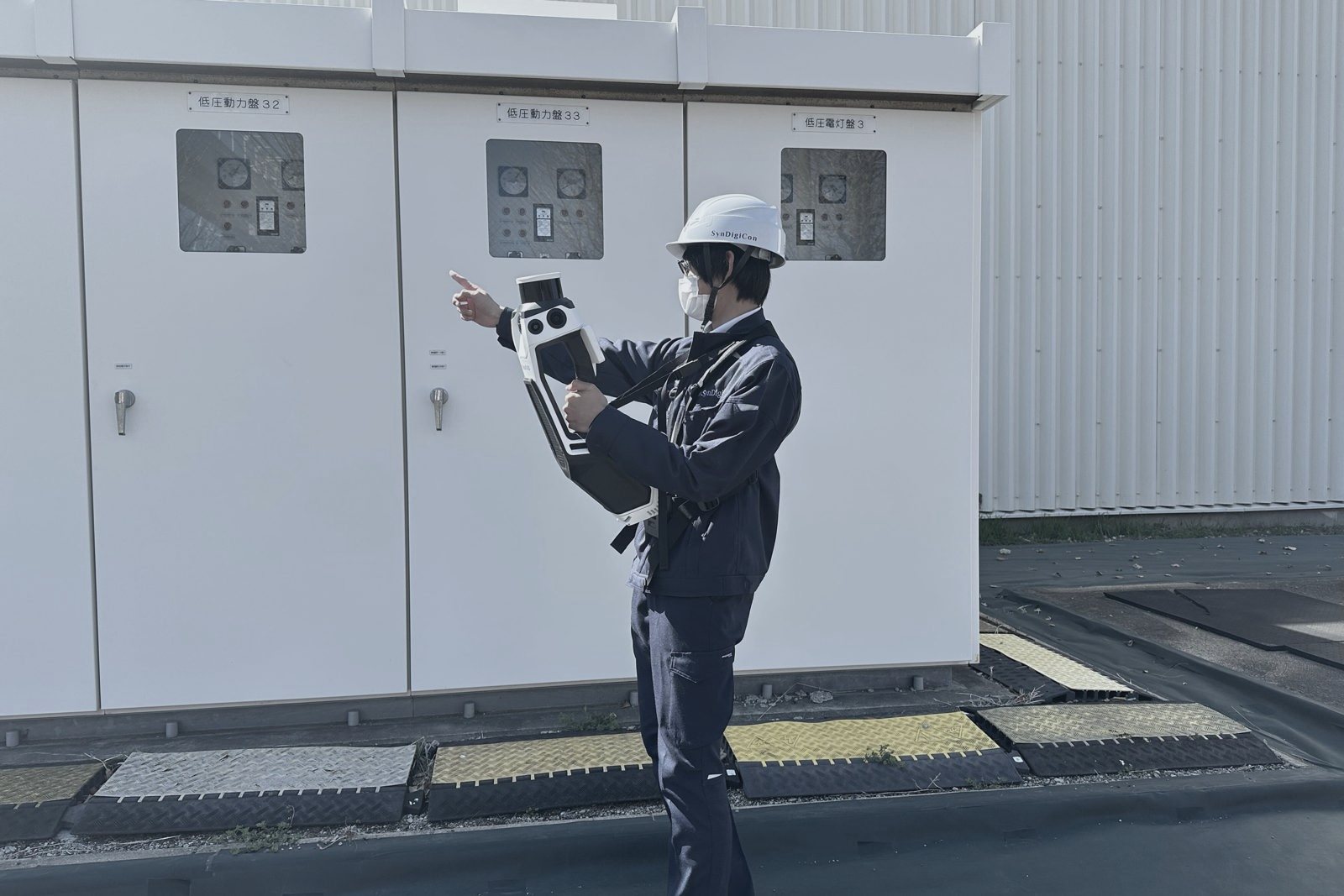 屋外の配電盤前で3Dスキャナを使う社員